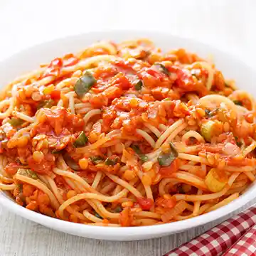 Spaghetti mit veganer Linsen-Bolognese aus roten Linsen, Möhren, Lauchzwiebeln und Tomaten, serviert auf einem weißen Teller.