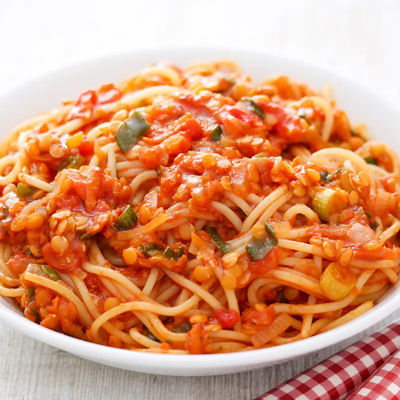 Vegane Linsenbolognese mit Spaghetti in Nahaufnahme, angerichtet auf einem weißen Teller.