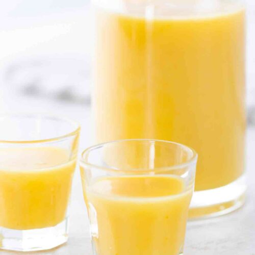 Eine Flasche mit veganem Eierlikör im Hintergrund, zwei kleine Gläser im Vordergrund.