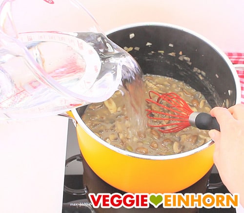 Wasser zu veganer Champignonsuppe im Topf zufügen
