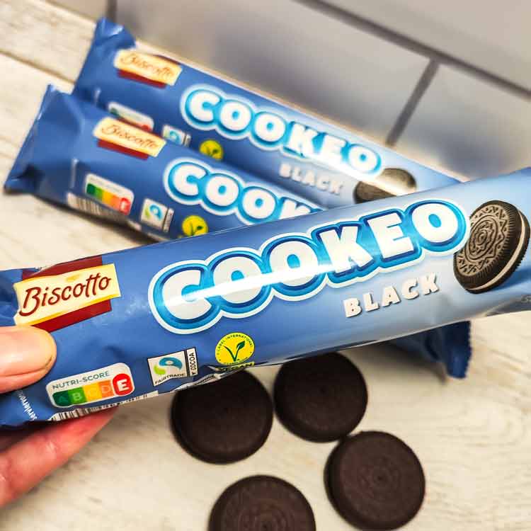 Eine Hand hält eine Packung Cookeo Black Kekse von Aldi, im Hintergrund weitere Kekspackungen und Kekse.