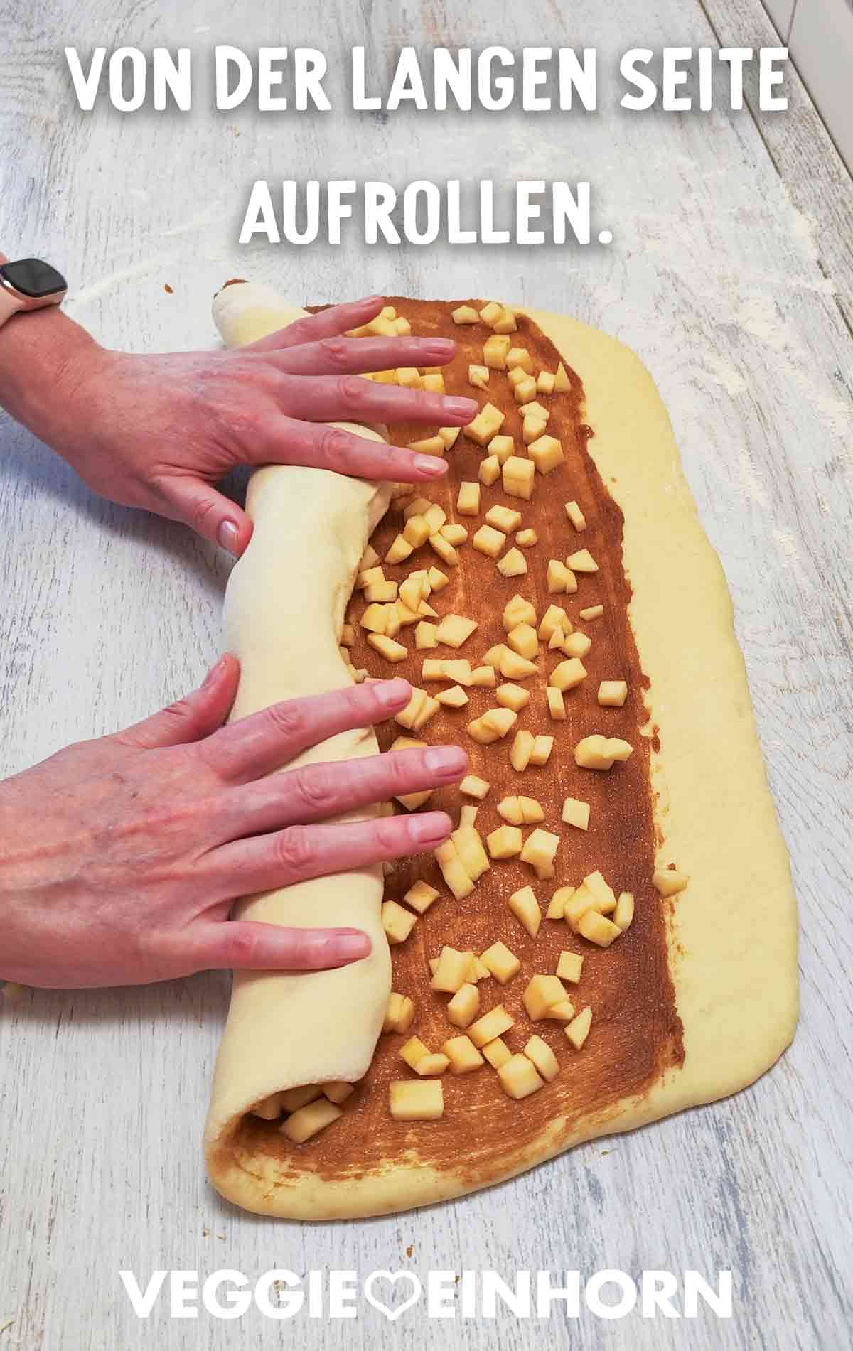 Hände rollen den Apfel-Zimt-Hefeteig von der langen Seite her auf.
