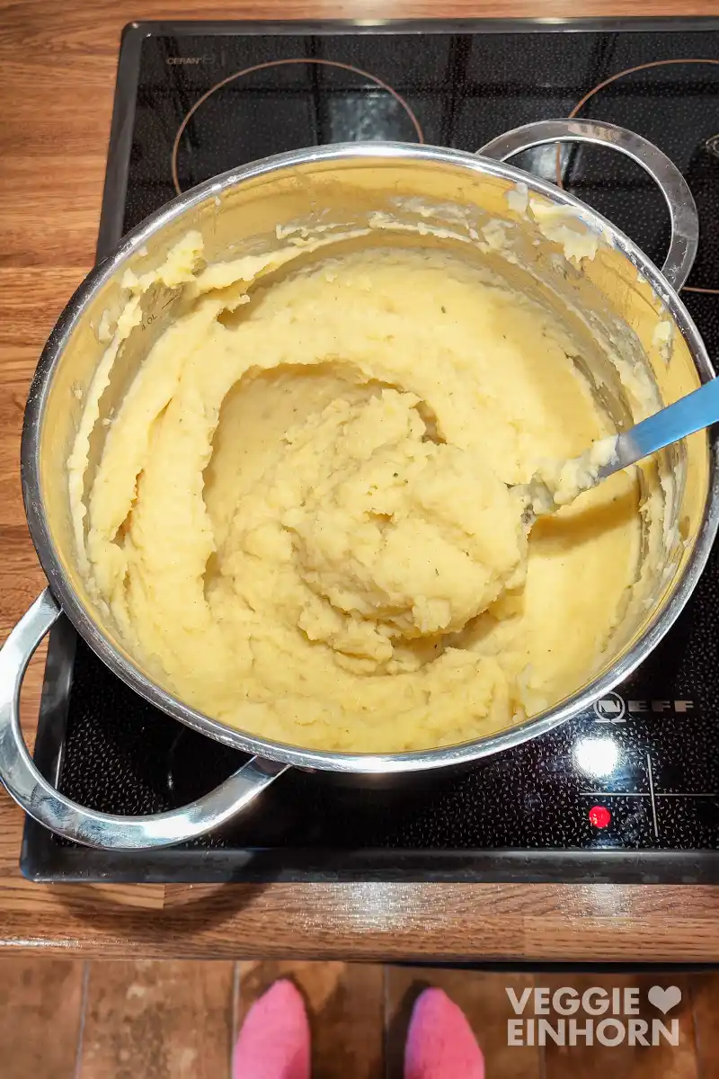 Veganer Kartoffelbrei in einem großen Topf auf dem Herd, mit einem Löffel im Püree.