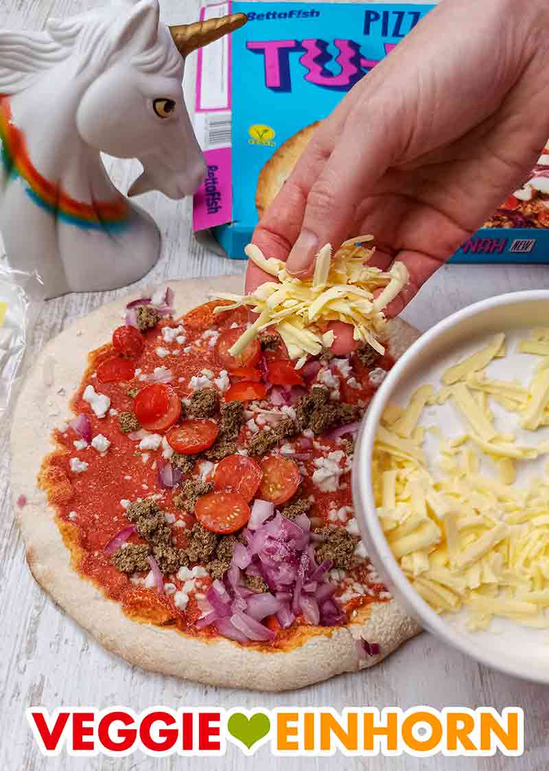 Die vegane Thunfisch Pizza wird mit geriebenem veganen Käse bestreut
