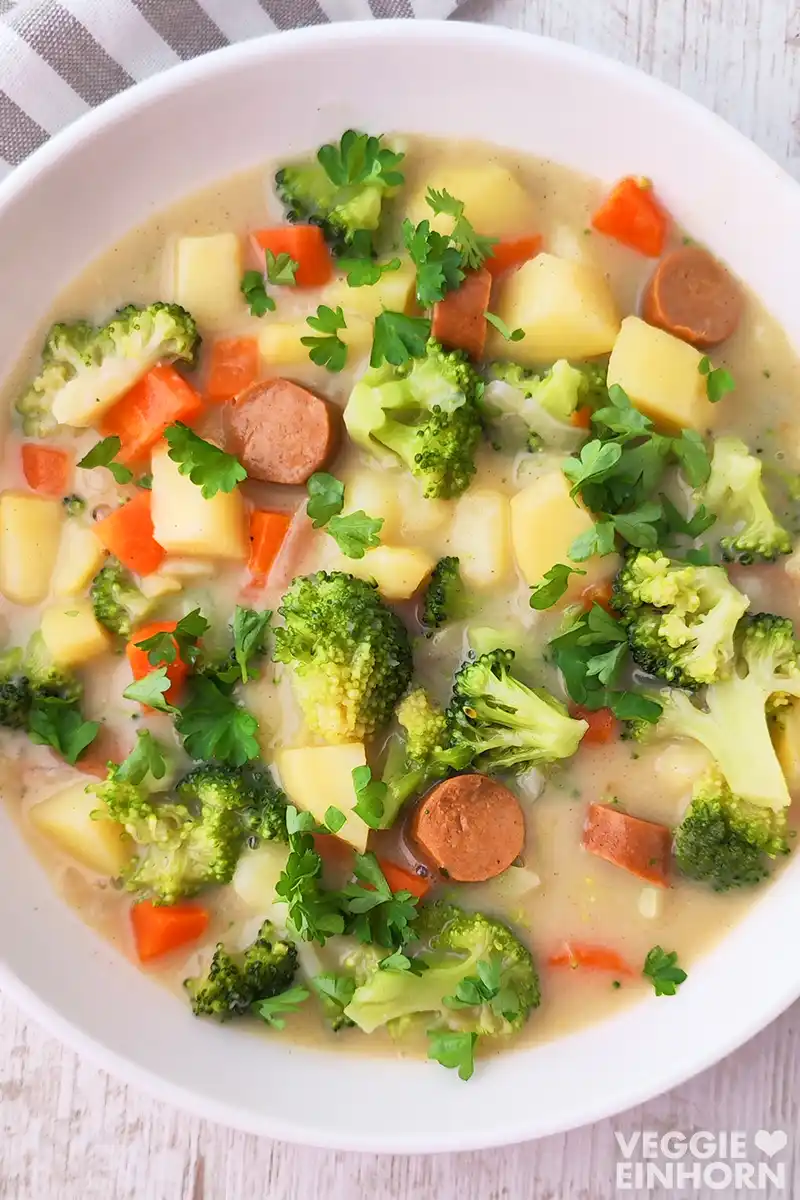 Gemüseeintopf mit veganen Wiener Würstchen Nahaufnahme von veganem Gemüseeintopf mit Brokkoli, Möhren, Kartoffeln und veganen Wiener Würstchen, bestreut mit frischer Petersilie.