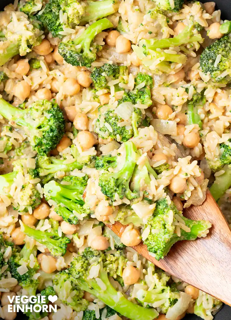 Vegane Brokkoli-Reis-Pfanne mit Kichererbsen in einer schwarzen Pfanne, angerichtet mit einem Holzlöffel.