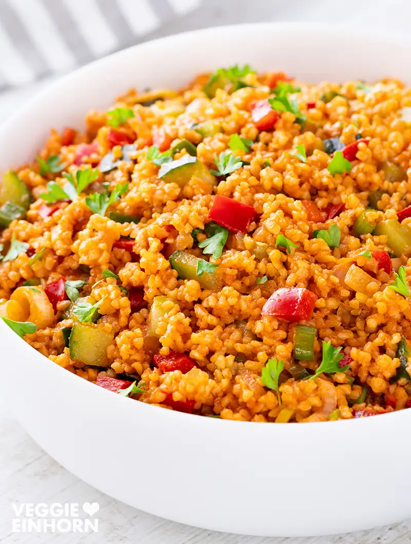 Veganer Bulgursalat mit Paprika, Gurke, Frühlingszwiebeln und Petersilie in einer weißen Schüssel.