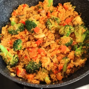Couscous mit buntem Gemüse, darunter Brokkoli, Paprika und Pilze, frisch gekocht in einer schwarzen Pfanne.