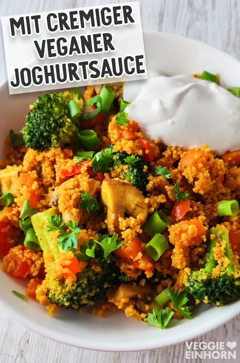 Bunte Couscouspfanne mit Gemüse, serviert mit cremiger veganer Joghurtsauce und bestreut mit Frühlingszwiebelringen und frischer Petersilie.