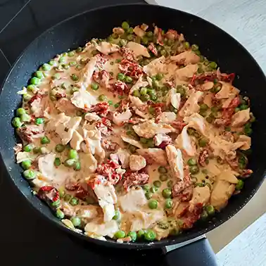 Vegane Hähnchenpfanne mit cremiger Sauce, Erbsen und getrockneten Tomaten in einer schwarzen Pfanne.