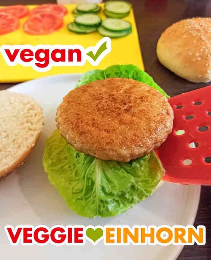 Ein veganer Sieht-Chick-Aus Burger Patty wird auf ein Burgerbrötchen mit einem Salatblatt gelegt.