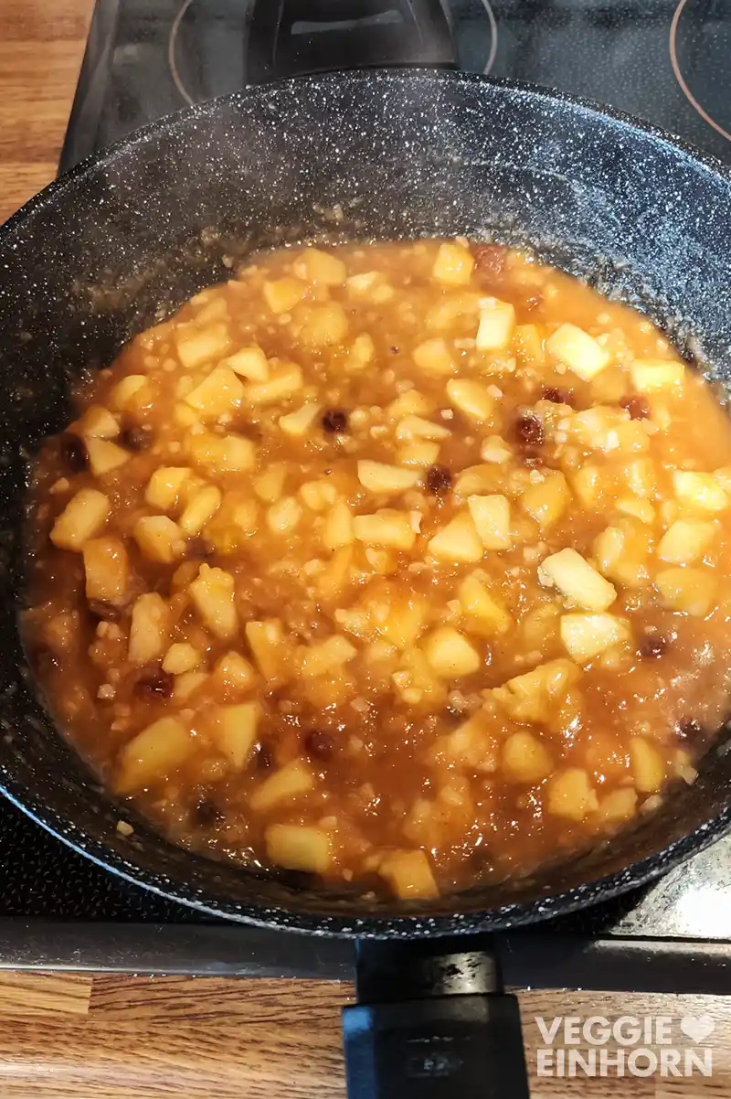 Pfanne mit frisch gekochter veganer Bratapfelsoße mit Apfelstückchen, Rosinen und Mandeln auf dem Herd.