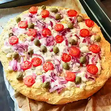 Frisch gebackene vegane Hummus-Pizza mit veganem Feta, Kirschtomaten, roten Zwiebeln und grünen Oliven auf Backpapier.