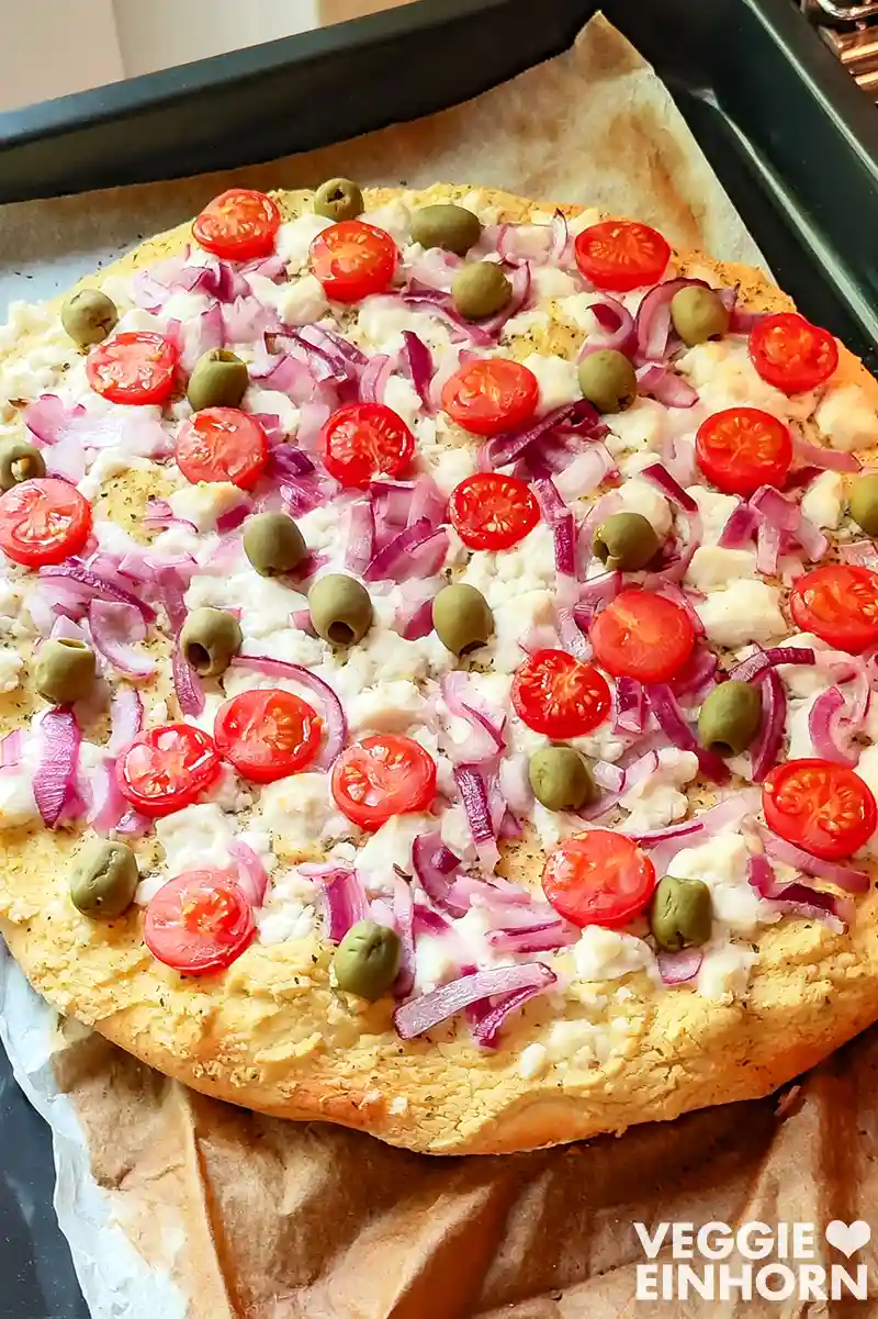 Nahaufnahme einer veganen Pizza mit Hummus, veganem Feta, Zwiebeln, Tomaten und Oliven.