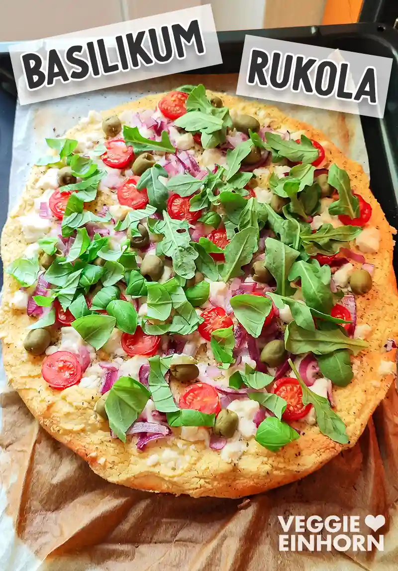 Vegane Hummus-Pizza nach dem Backen, frisch belegt mit Rucola und Basilikum.