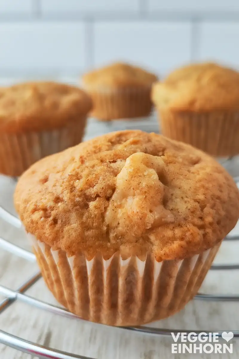 Vier goldbraune vegane Apfel Muffins auf einem runden Kuchengitter.