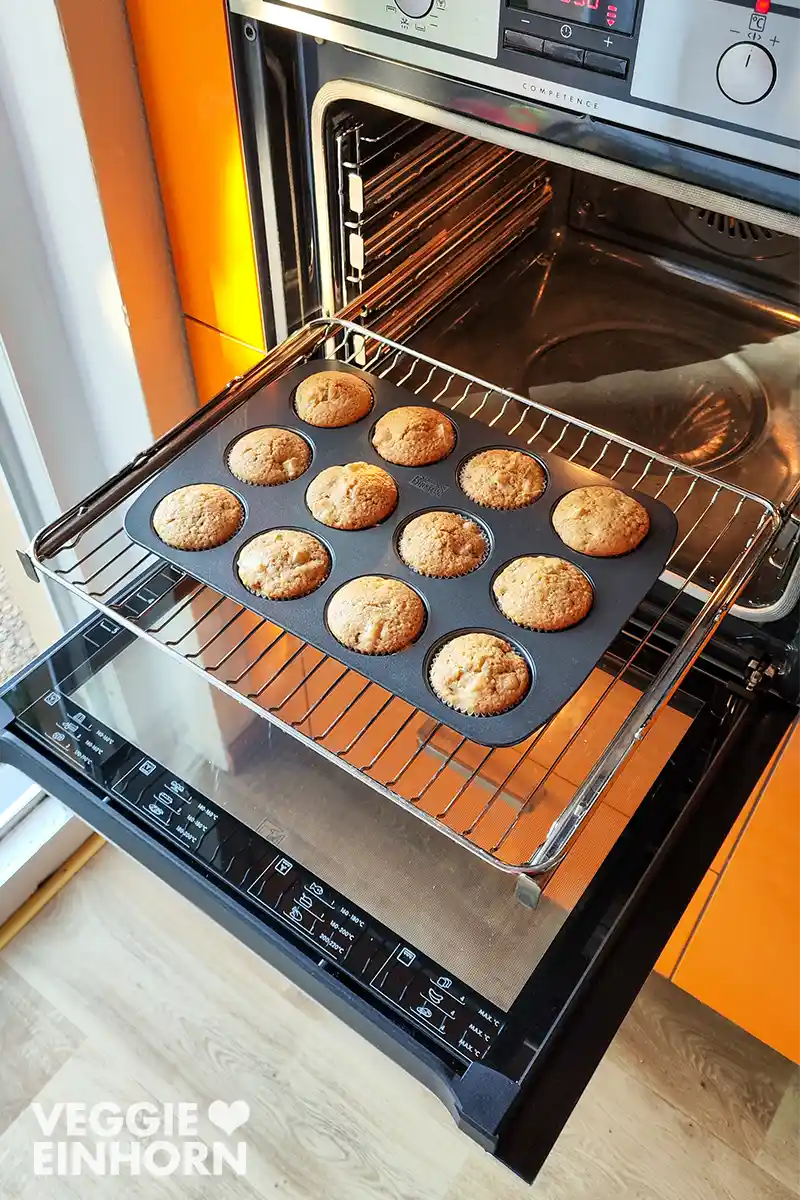 Eine Muffinform mit 12 veganen Apfelmuffins steht im geöffneten Backofen.