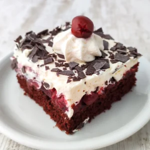 Ein Stück vegane Schwarzwälder Kirschtorte vom Blech auf einem weißen Teller mit Schokoraspeln, Sahne und einer Kirsche als Topping.