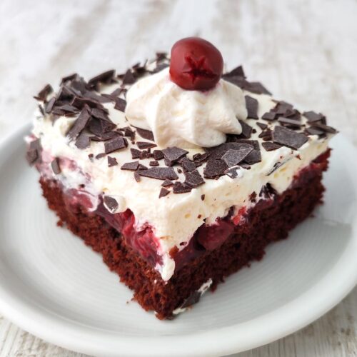 Ein einzelnes Stück vegane Schwarzwälder Kirschtorte vom Blech mit lockerer Schokoschicht, Kirschfüllung, Sahnehaube und Schokoraspeln.