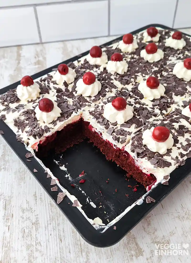 Kuchenblech mit einer angeschnittenen veganen Schwarzwälder Kirschtorte.