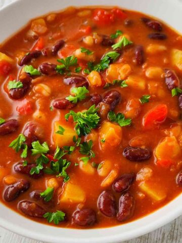 Nahaufnahme eines veganen Bohneneintopfs mit Kartoffeln, garniert mit frischer Petersilie.