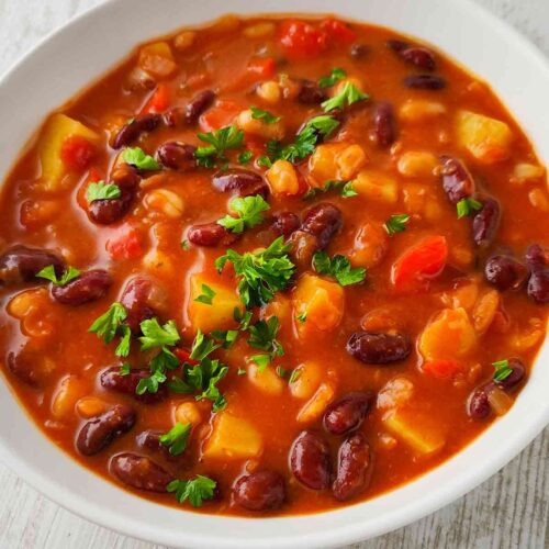 Nahaufnahme eines veganen Bohneneintopfs mit Kartoffeln, garniert mit frischer Petersilie.