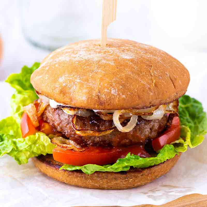 Veganer Burger mit Patty, Salat, Tomatenscheiben, gebratenen Zwiebeln, veganem Ketchup und veganer Mayo im Brötchen.