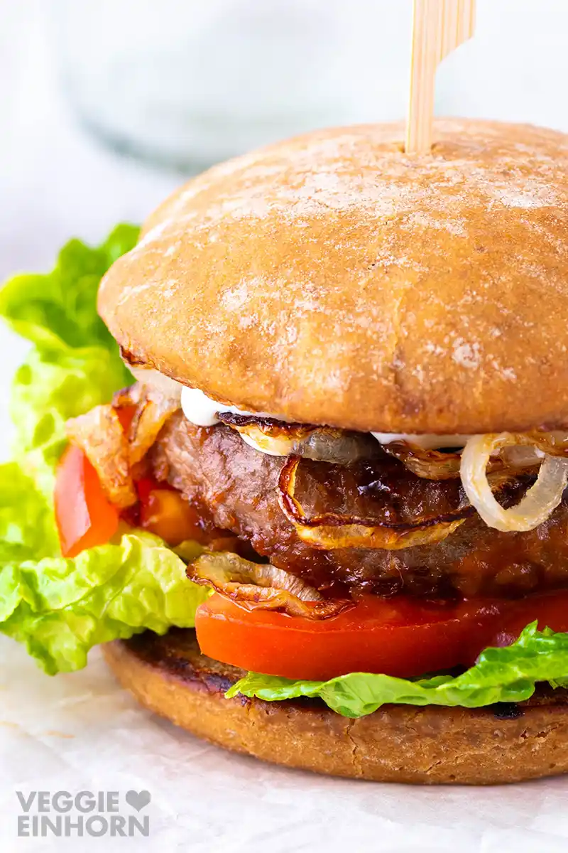Nahaufnahme eines veganen Burgers mit grünem Salat, Tomatenscheiben, Patty, gebratenen Zwiebeln und Burgerbrötchen.