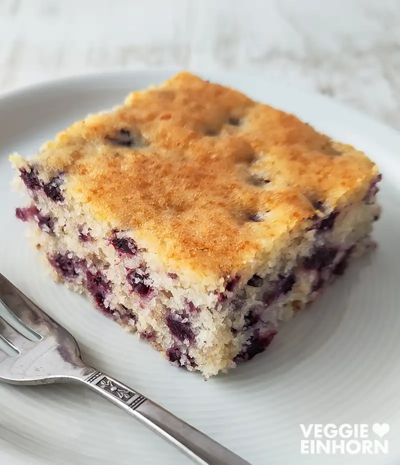 Nahaufnahme von einem Stück veganen Heidelbeerkuchen vom Blech auf einem weißen Kuchenteller.