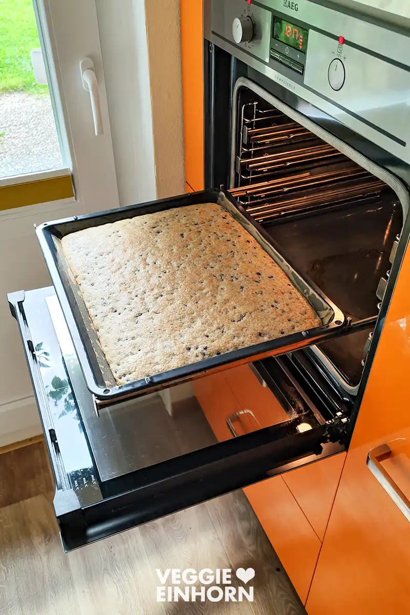 Backblech mit veganem Heidelbeerkuchen vor dem geöffneten Backofen.
