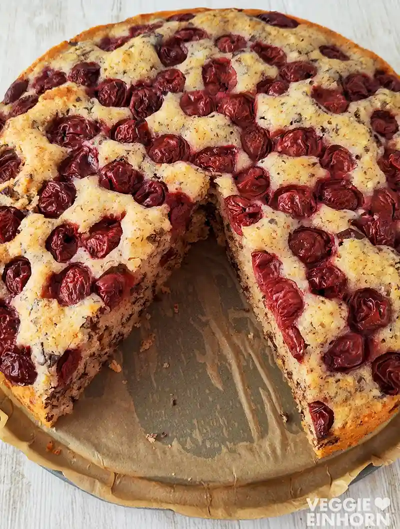 Nahaufnahme eines angeschnittenen veganen Nusskuchens mit Kirschen und Schokolade.