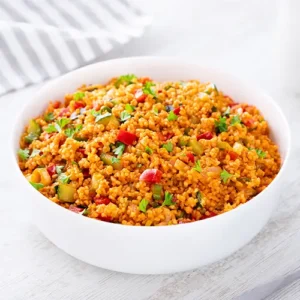 Weiße Schüssel mit veganem Bulgursalat auf hellem Untergrund, im Hintergrund ein gestreiftes Tuch