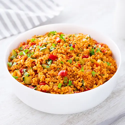 Weiße Schüssel mit veganem Bulgursalat auf hellem Untergrund, im Hintergrund ein gestreiftes Tuch