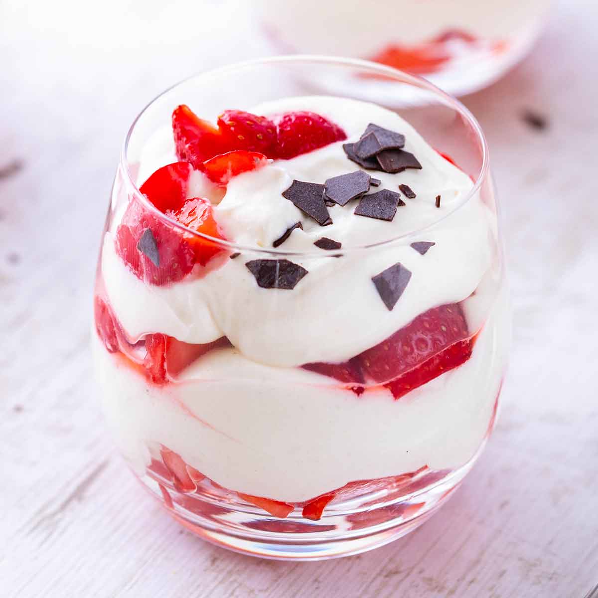 Glas mit veganem Erdbeer-Dessert, geschichtet mit frischen Erdbeeren, veganer Dessertcreme und Schokoraspeln.