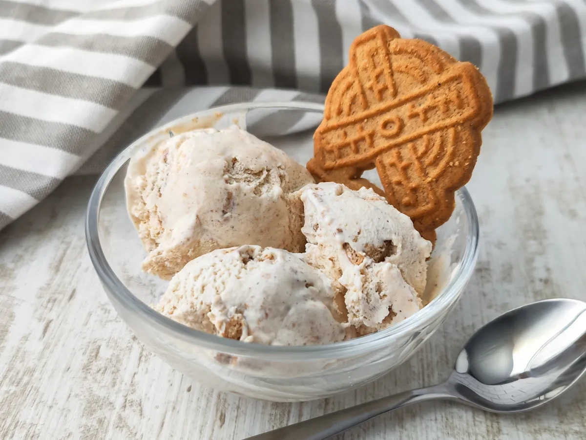 Veganes Spekulatius Eis in einer Glasschale mit einem Spekulatiuskeks und einem Löffel auf hellem Holztisch serviert.
