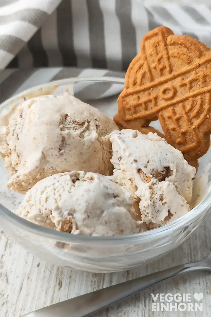 Nahaufnahme von cremigem veganem Spekulatius Eis mit einem Spekulatius in einer Glasschale auf hellem Holztisch.