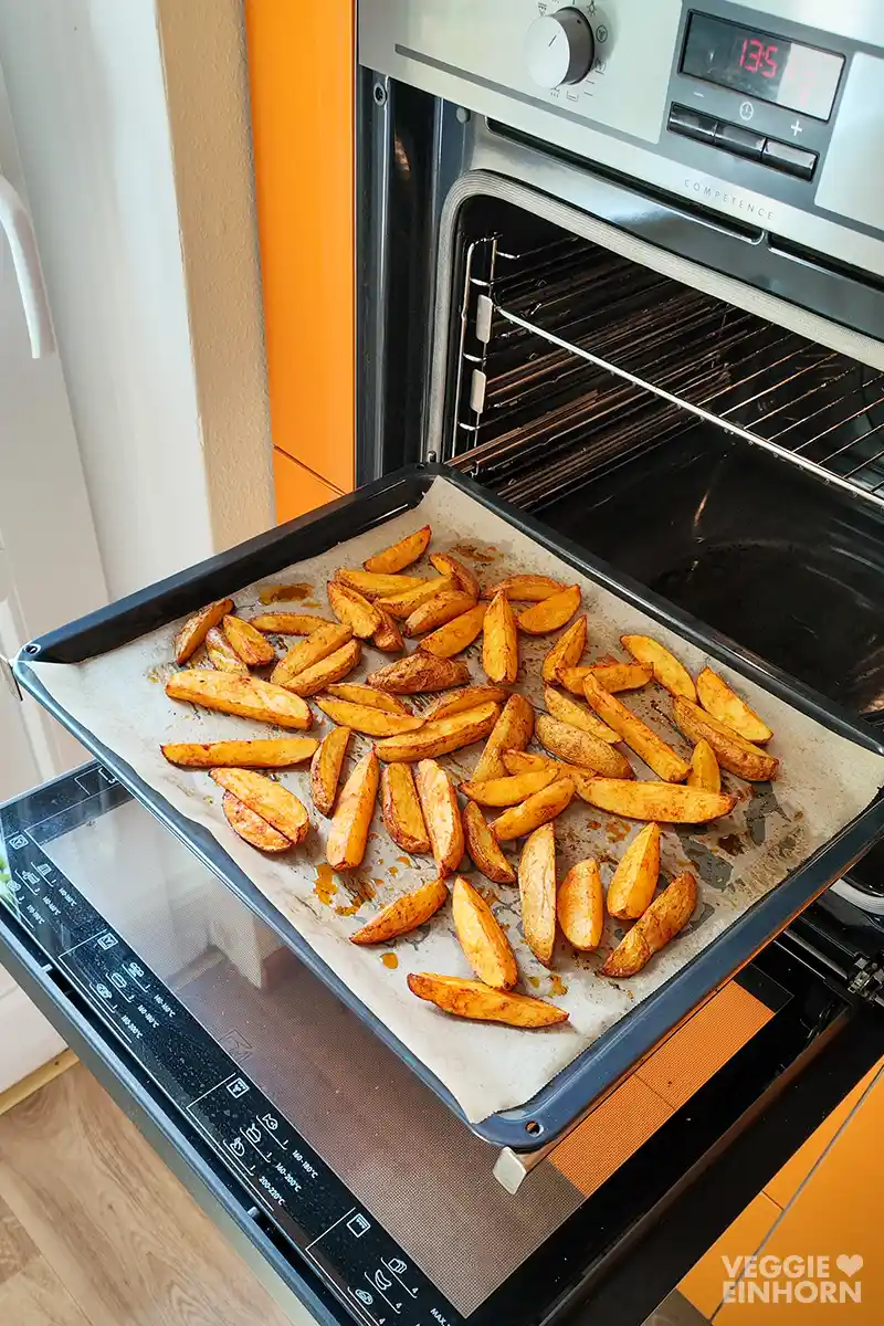 Ofengebackene Kartoffel Wedges im geöffneten Backofen auf einem Backblech verteilt.