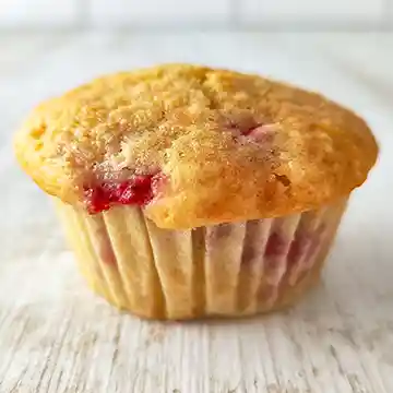 Ein veganer Erdbeermuffin in einem Papierförmchen auf hellem Holzuntergrund, leicht von schräg oben fotografiert.