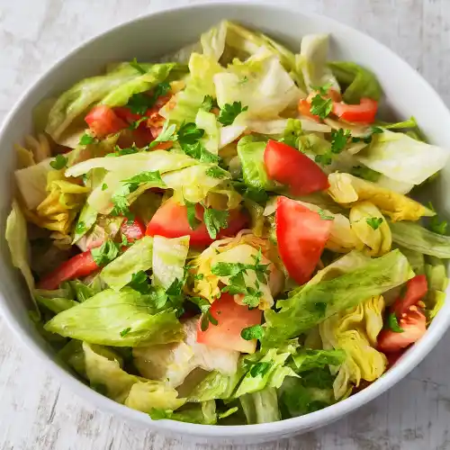 Einfacher Eisbergsalat mit Tomaten in einer weißen Schüssel, bestreut mit frischer Petersilie.