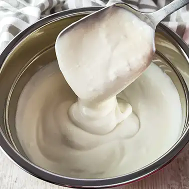 Schüssel mit cremiger veganer Joghurtsoße, ein Löffel mit Soße wird aus der Schüssel gehoben.