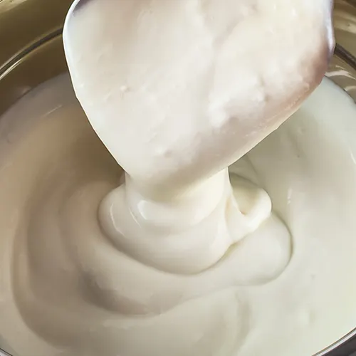 Nahaufnahme von cremiger veganer Joghurtsoße in einer Schüssel und auf einem Löffel.