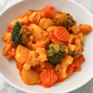 Veganes Gemüsecurry mit Kartoffeln, Kokosmilch und roten Linsen auf einem weißen Teller.