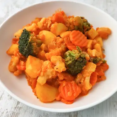 Veganes Gemüsecurry mit Kokosmilch, Kartoffeln und roten Linsen auf einem weißen Teller.