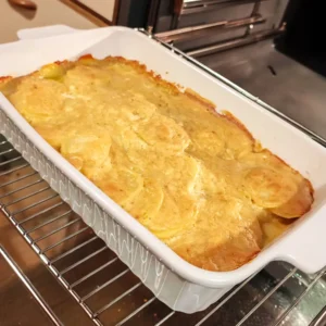 Goldbraun überbackenes veganes Kartoffelgratin in einer weißen Auflaufform auf dem Ofenrost.