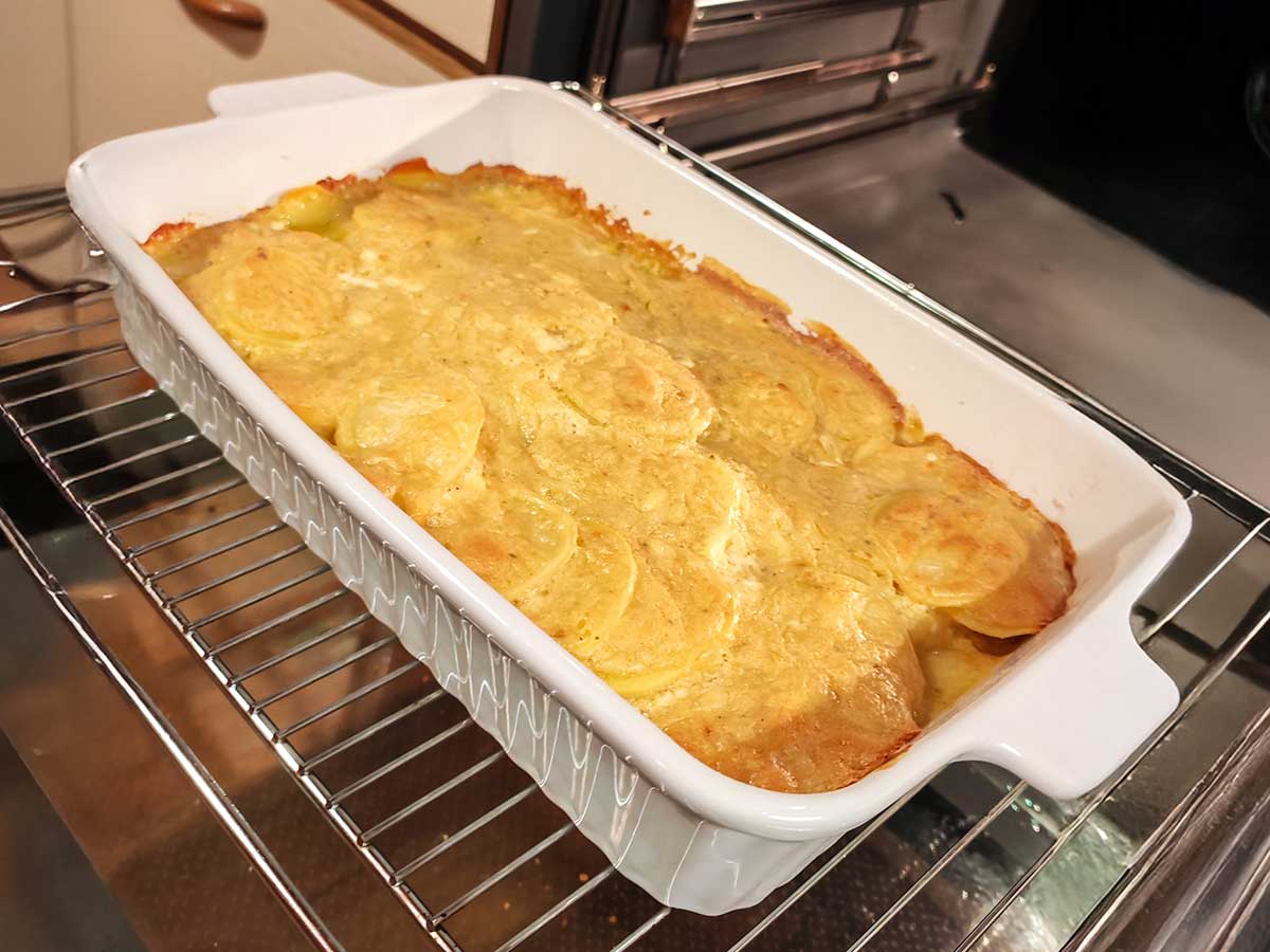 Veganes Kartoffelgratin in einer weißen Auflaufform auf dem Ofengitter.