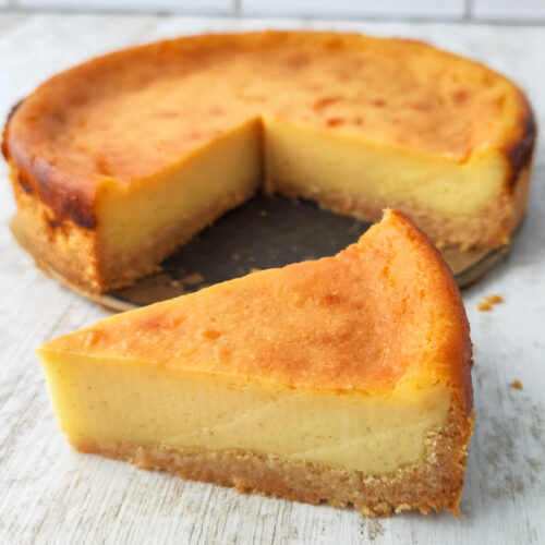 Kleiner veganer Käsekuchen mit goldbrauner Oberfläche, ein Stück ist herausgeschnitten und davor platziert.