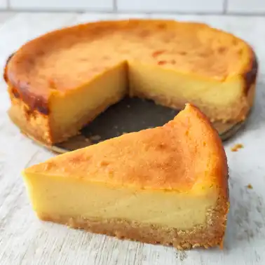 Kleiner veganer Käsekuchen mit goldbrauner Oberfläche, ein Stück ist herausgeschnitten und davor platziert.