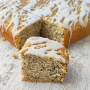 Veganer Zitronen-Mohnkuchen mit Zitronenglasur, ein Stück ist angeschnitten.