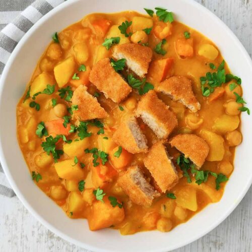 Vegane Nuggets auf Kürbis-Kichererbsen-Eintopf mit Kartoffeln und Petersilie, serviert in einer weißen Schüssel.