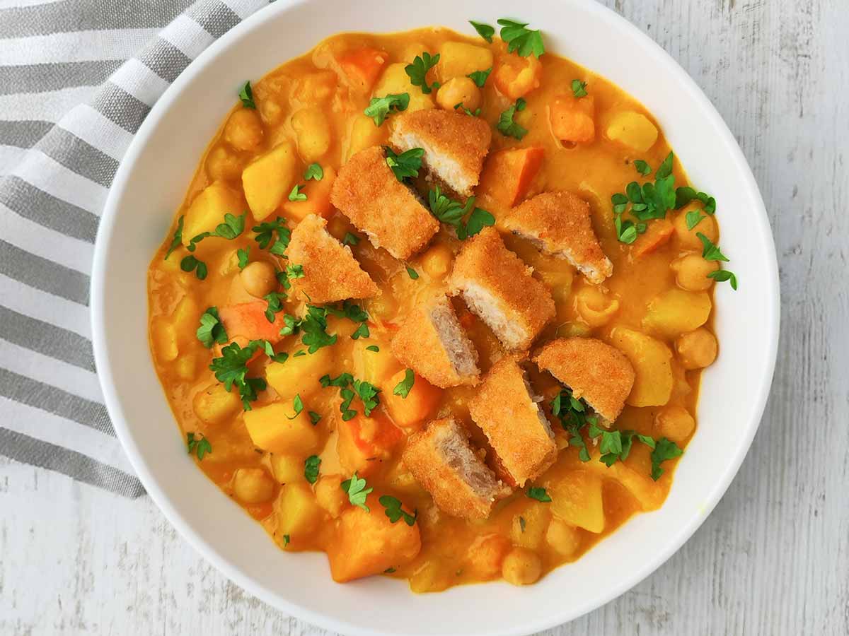 Vegane Nuggets auf Kürbis-Kichererbsen-Eintopf mit Kartoffeln und Petersilie, serviert in einer weißen Schüssel.